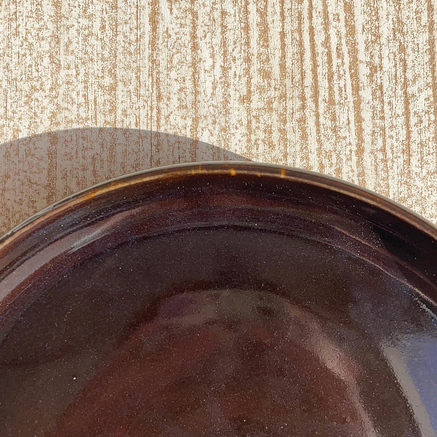 Close-up of a dark brown ceramic plate on a textured beige surface
