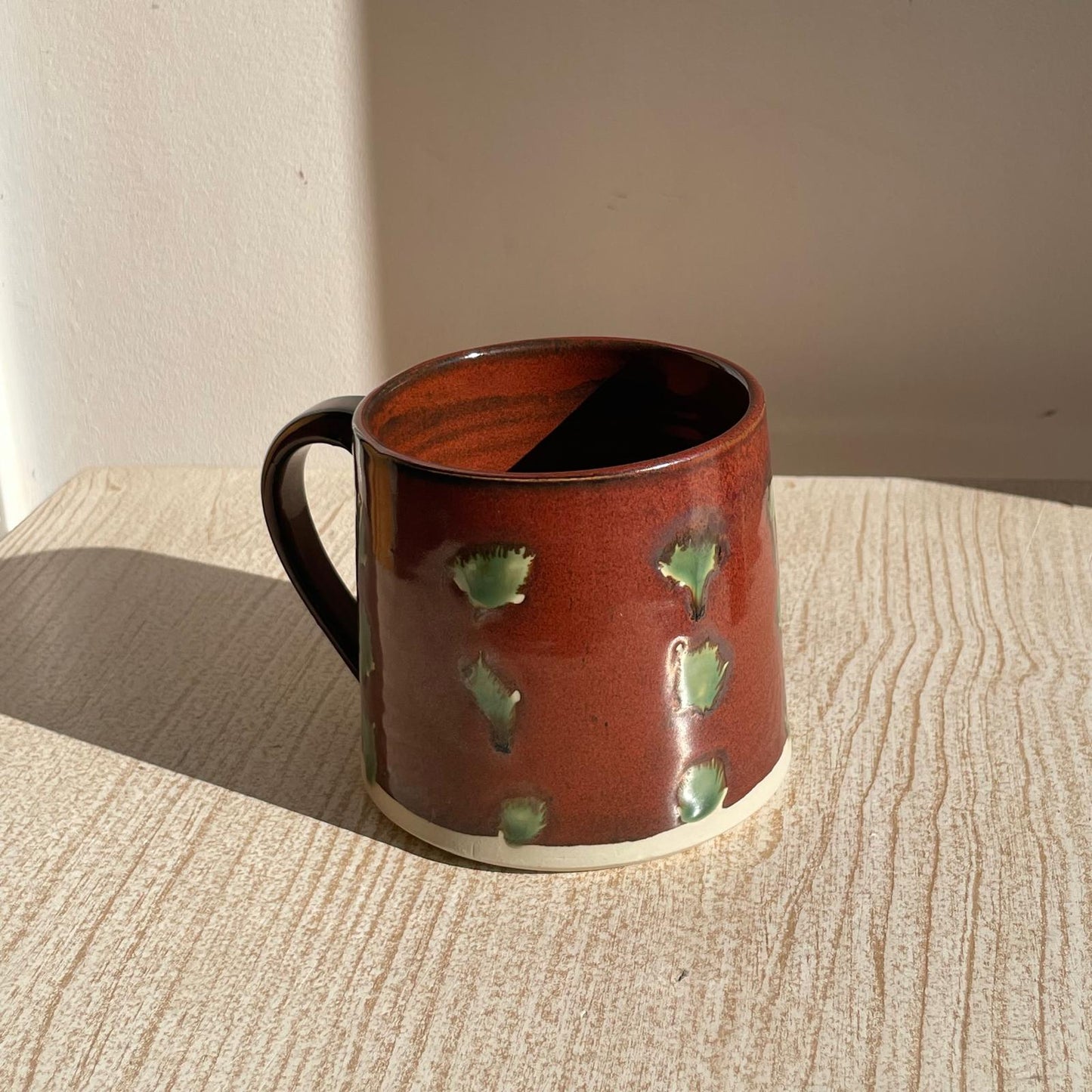 Brown ceramic mug with green patterns on a wooden surface