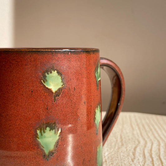 Red ceramic mug with green accents on a textured surface