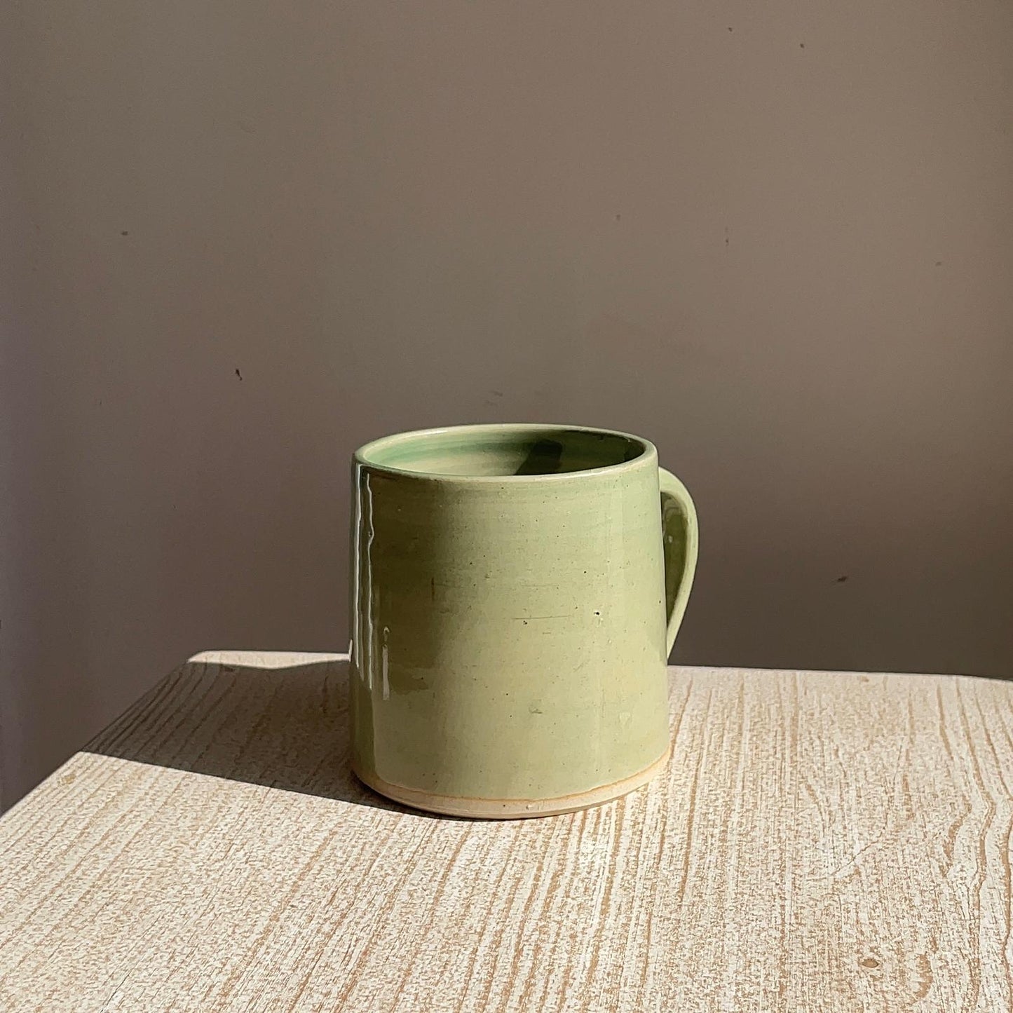 Green ceramic mug on a textured surface with a plain background