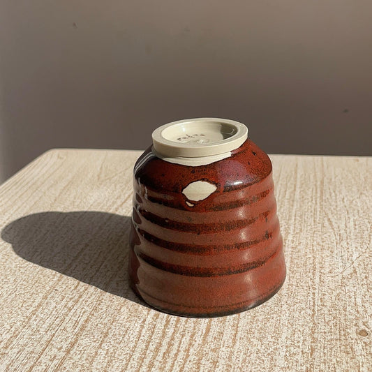 tenmoku red ceramic cup upside down on a textured surface with a neutral background