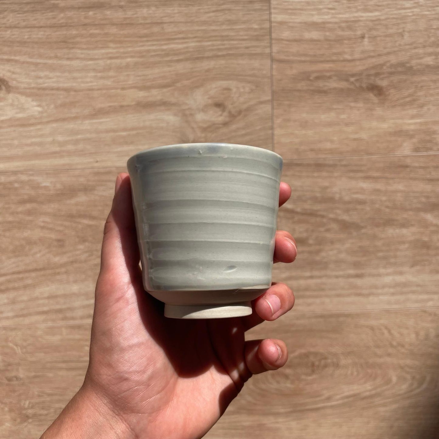 Hand holding a small ceramic cup against a wooden background
