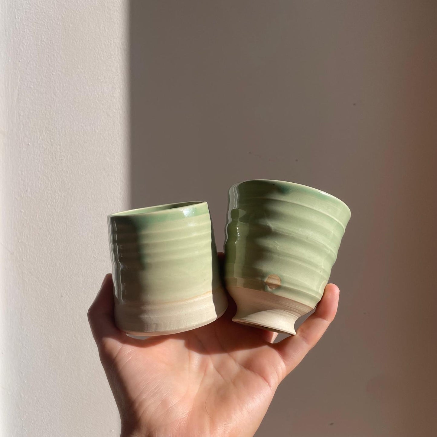 Two green ceramic cups held in a hand against a plain background