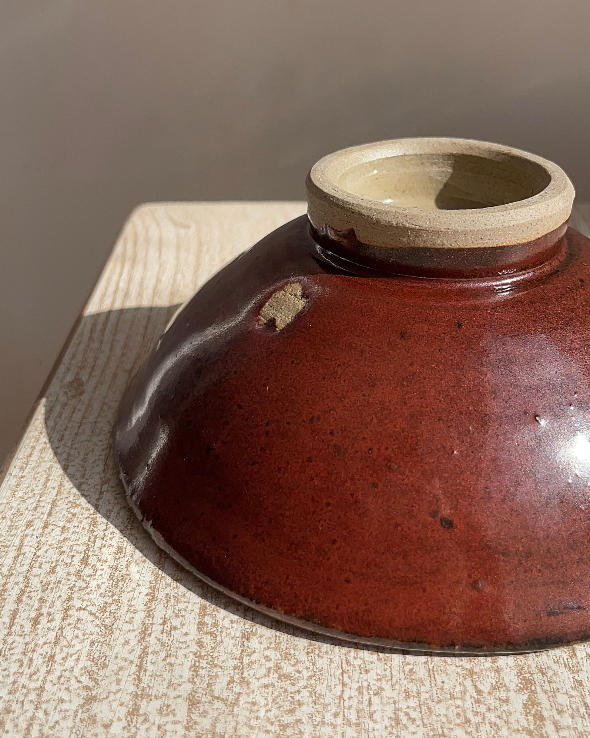 red ceramic bowl, uupside down, with a white rim on a wooden surface
