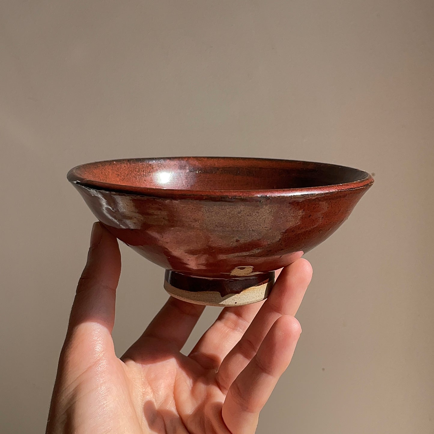 Hand holding a red ceramic bowl against a plain background