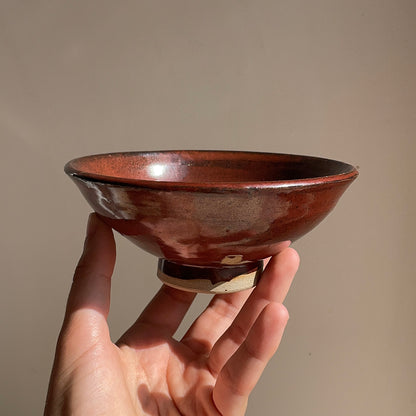 Hand holding a red ceramic bowl against a plain background