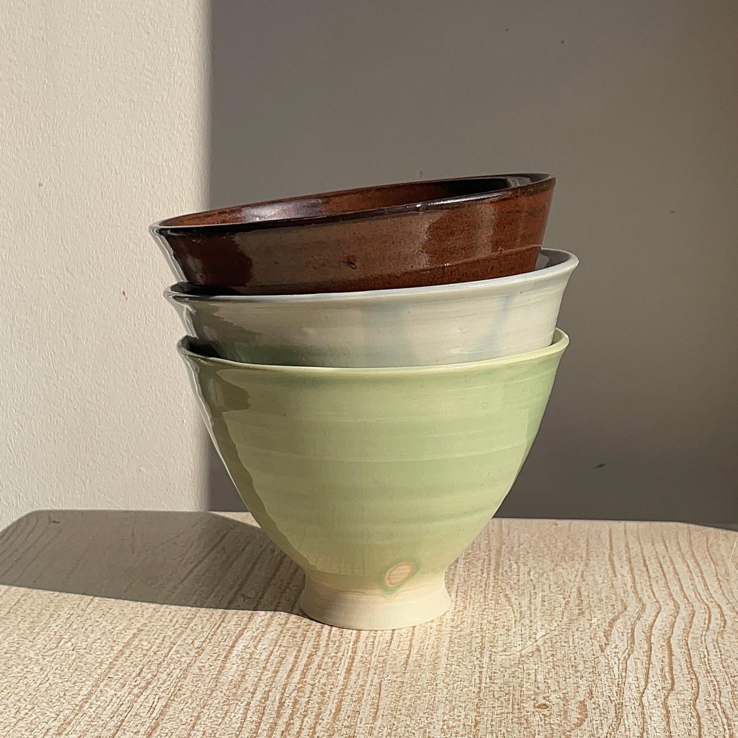 Stack of ceramic bowls in green, blue, and red on a wooden surface.