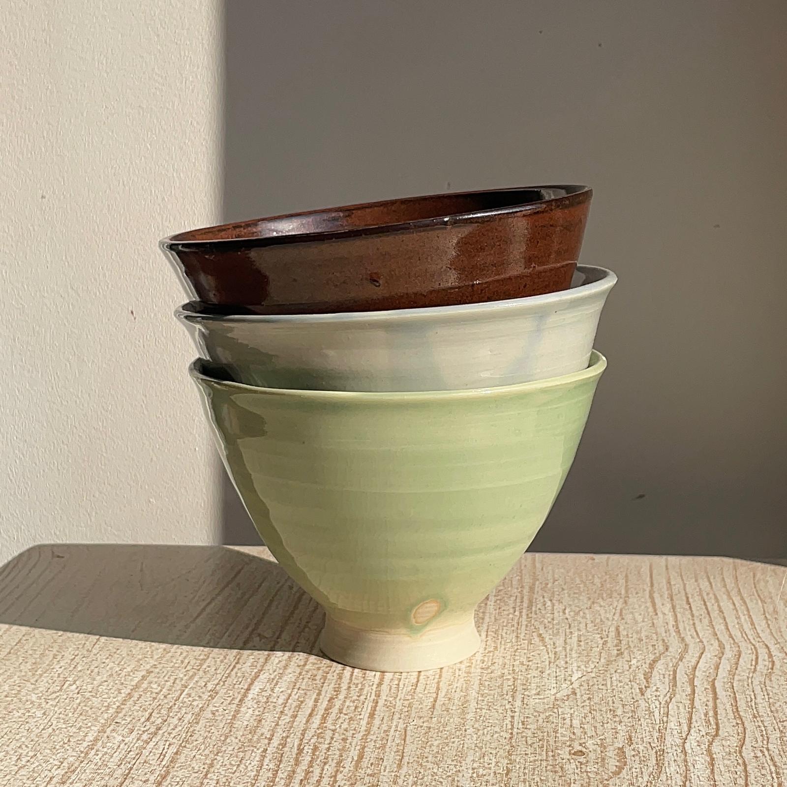 Stack of ceramic bowls in green, blue, and red on a wooden surface.