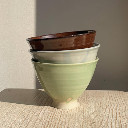 Stack of ceramic bowls in green, blue, and red on a wooden surface.