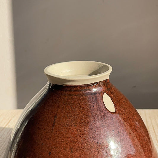 red ceramic vase with a white rim on a wooden surface