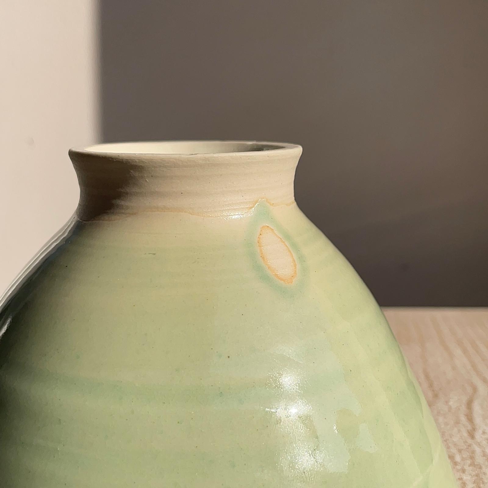 Green ceramic vase with a textured surface on a neutral background