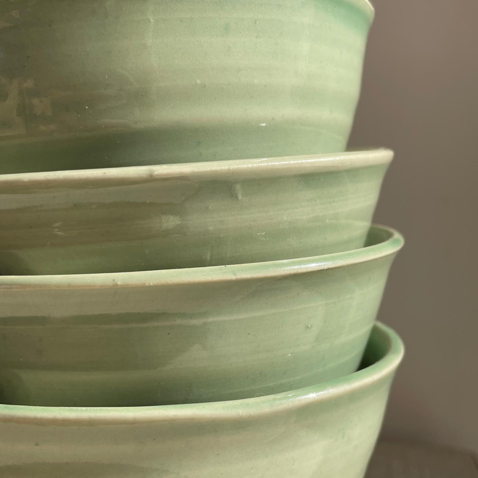 Stack of green ceramic bowls on a neutral background