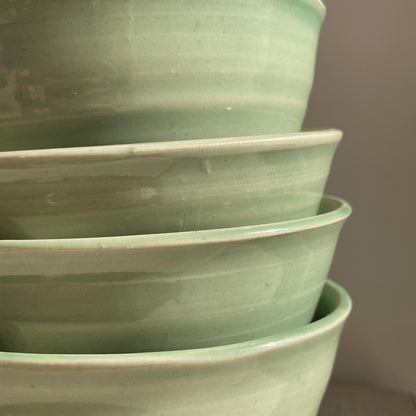 Stack of green ceramic bowls on a neutral background