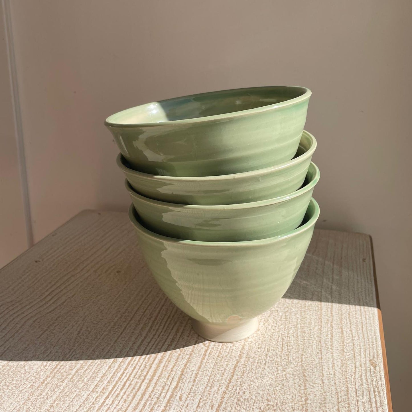 Stack of green ceramic bowls on a wooden surface with a neutral background
