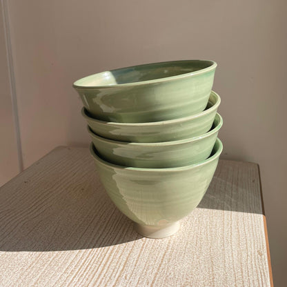 Stack of green ceramic bowls on a wooden surface with a neutral background