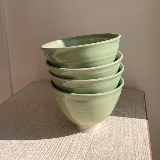 Stack of green ceramic bowls on a wooden surface with a neutral background