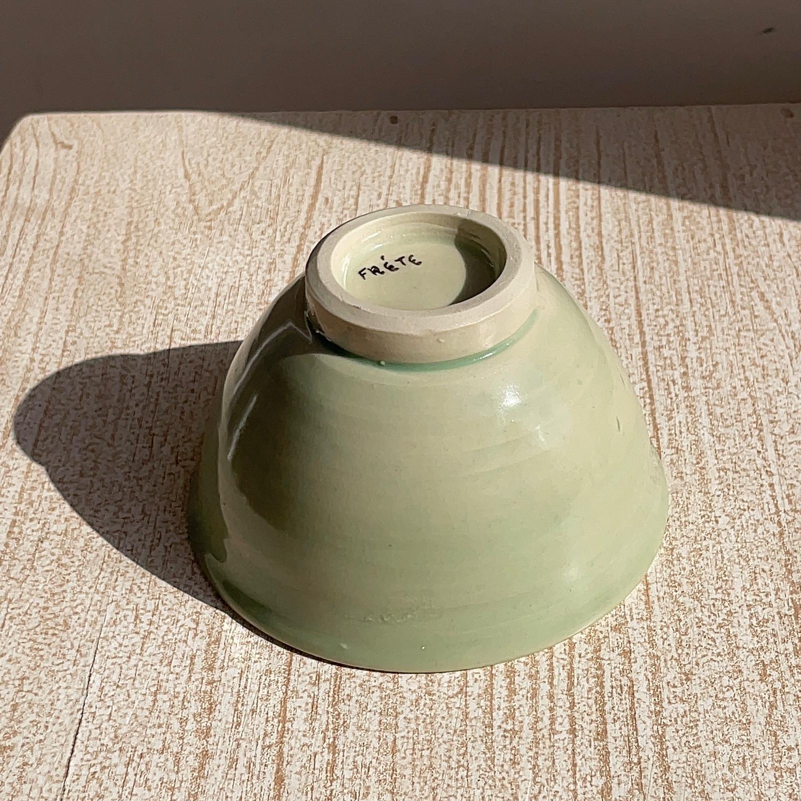 Green ceramic bowl on a textured surface with 'Frete' branding.
