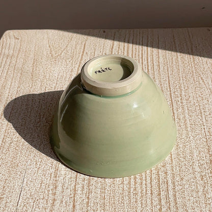 Green ceramic bowl on a textured surface with 'Frete' branding.