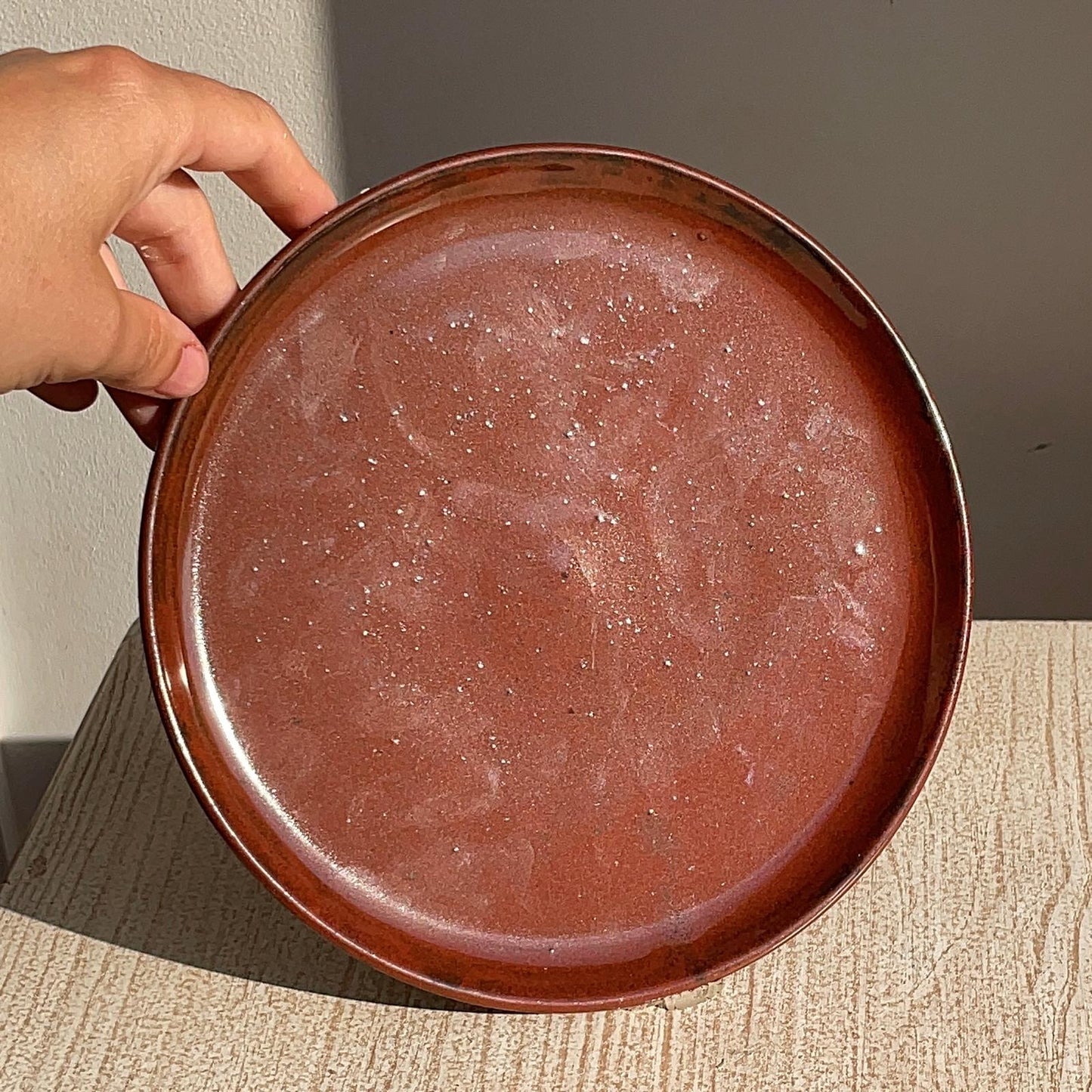 Hand holding a red ceramic plate on a neutral background