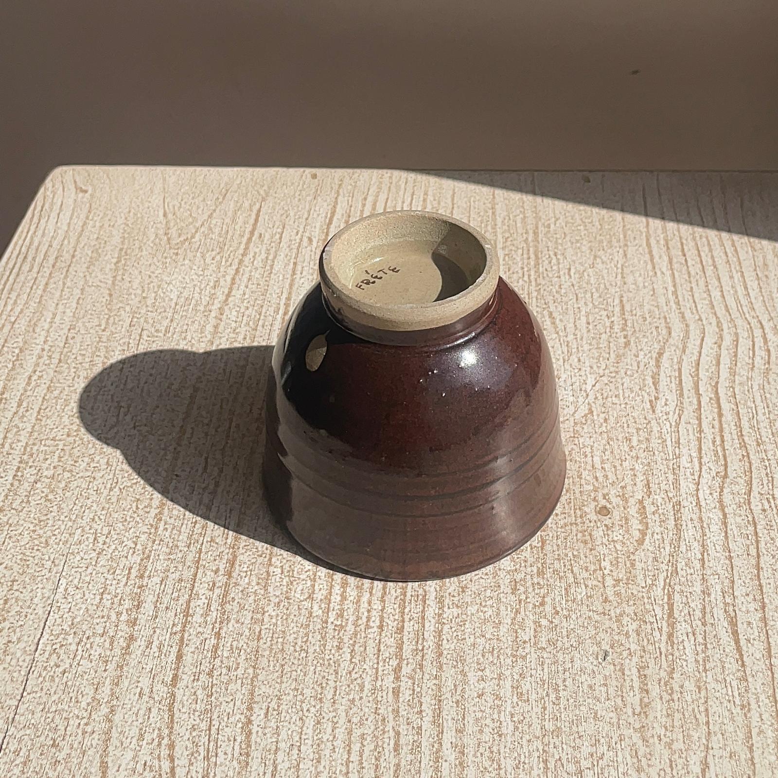 Brown ceramic cup with beige interior on a textured surface