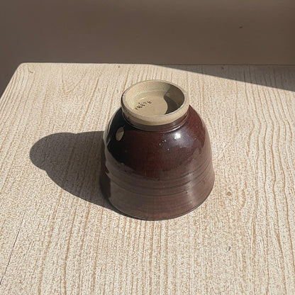 Brown ceramic cup with beige interior on a textured surface