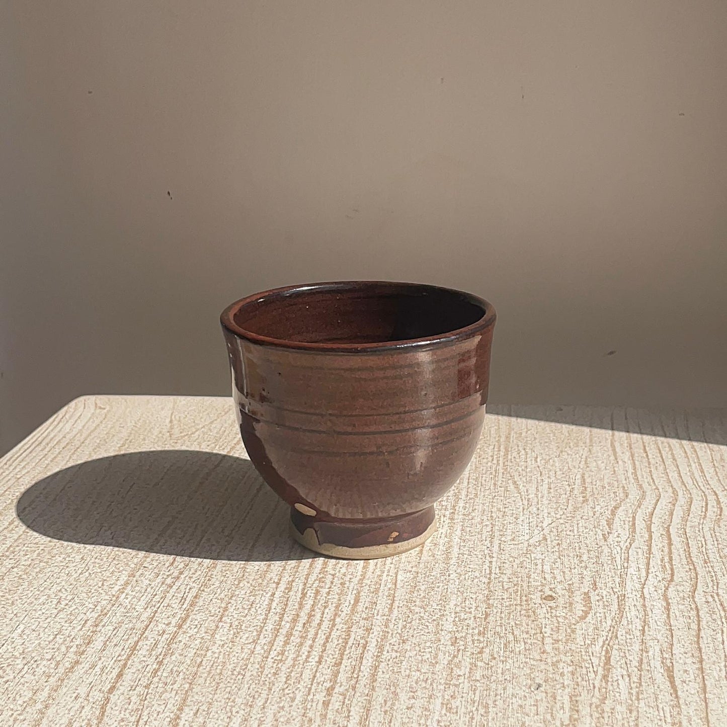 Brown ceramic pot on a textured surface with a neutral background