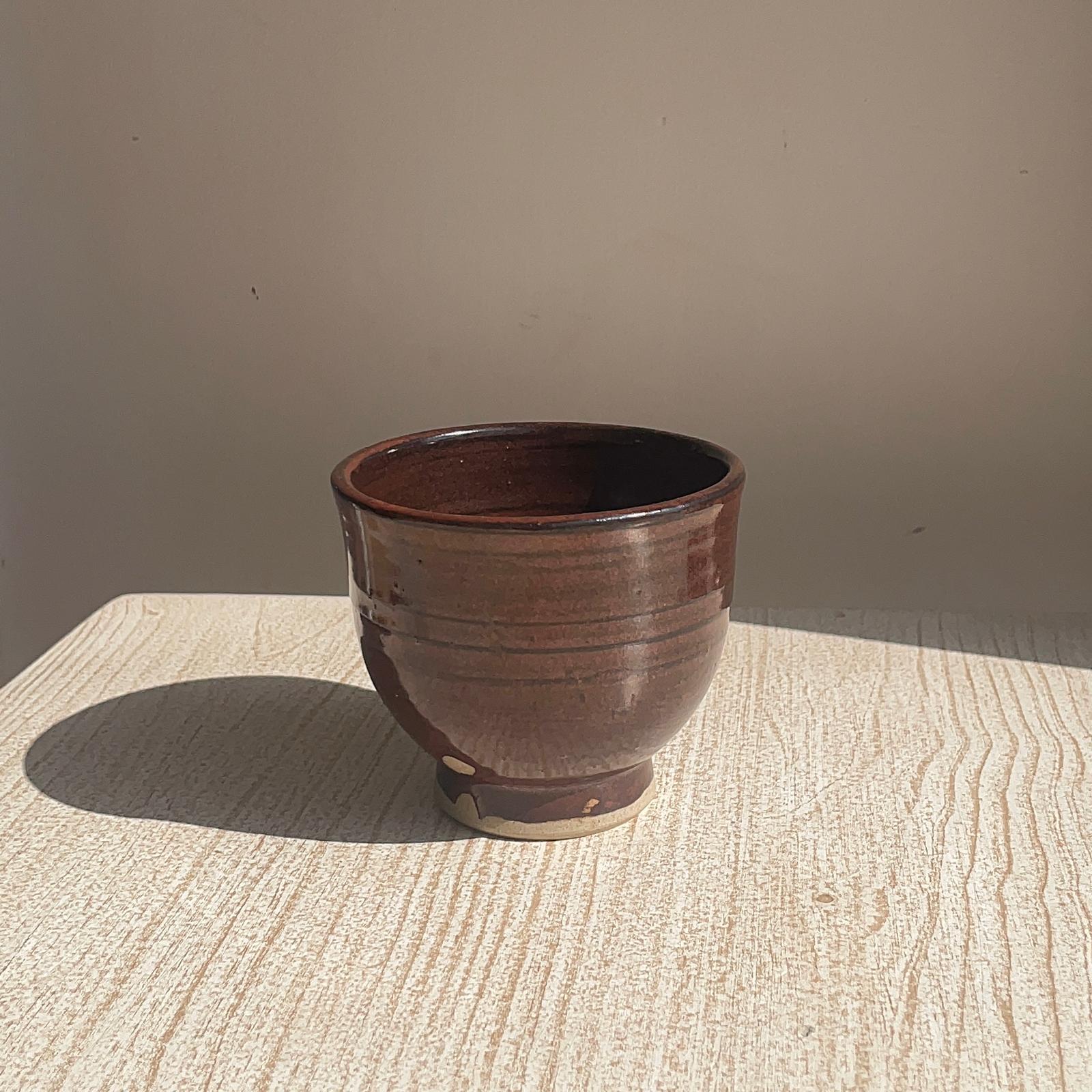 Brown ceramic pot on a textured surface with a neutral background