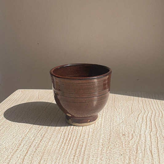 Brown ceramic pot on a textured surface with a neutral background