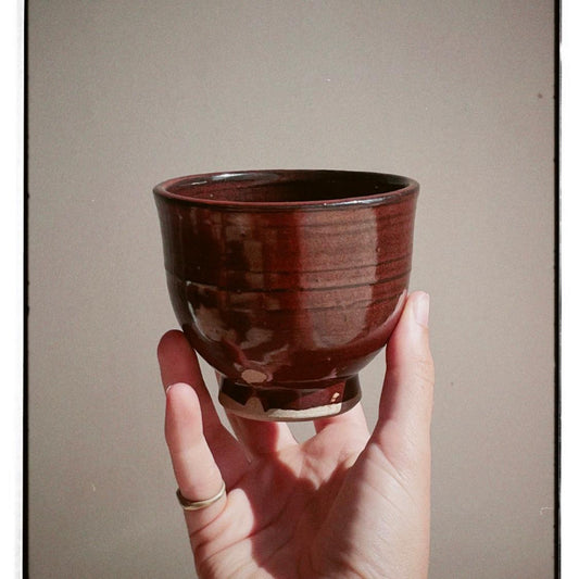 Hand holding a red ceramic cup against a plain background