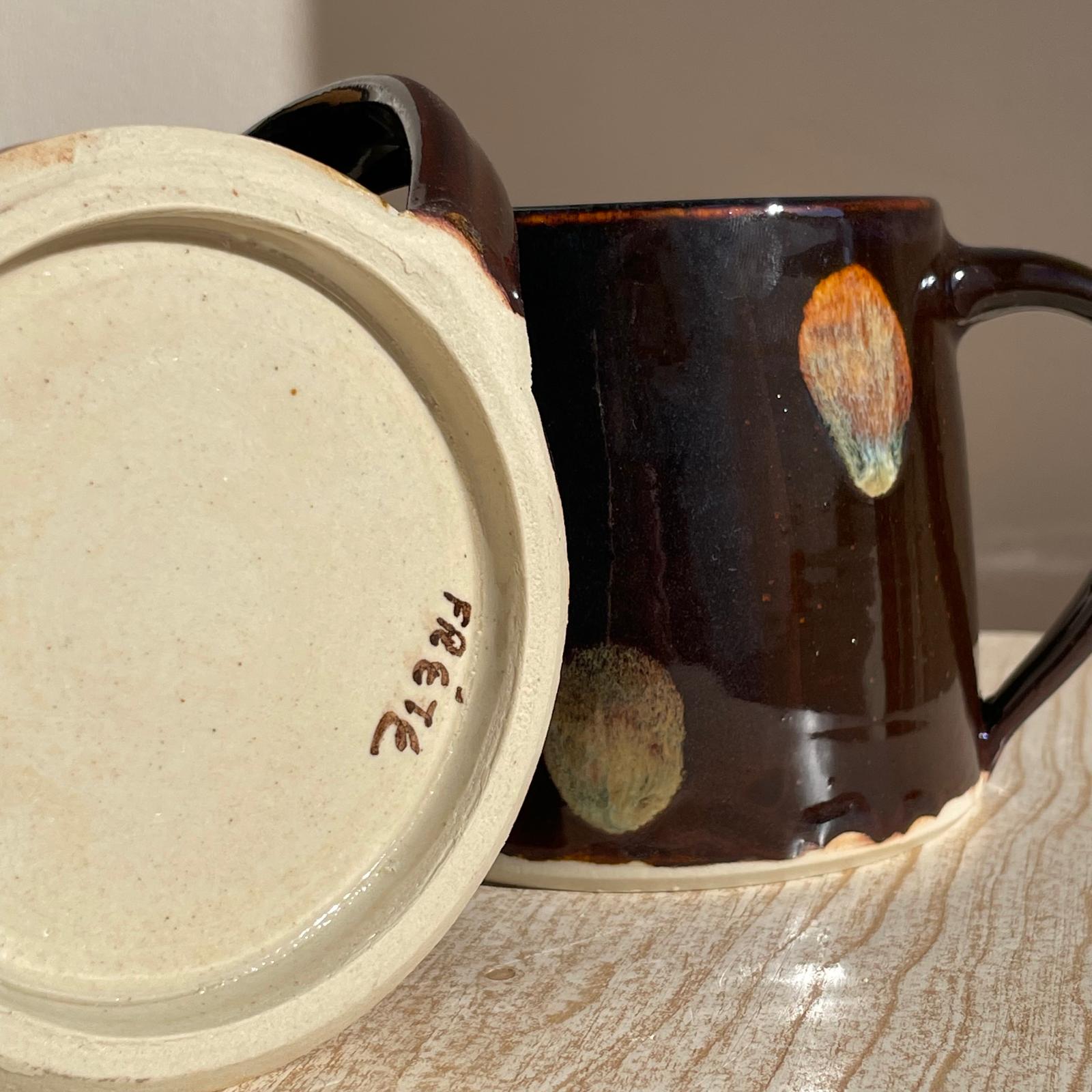 Close-up of a ceramic mug with a decorative handle and a beige bottom on a wooden surface.