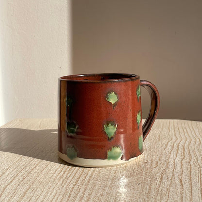 Red ceramic mug with green spots on a wooden surface