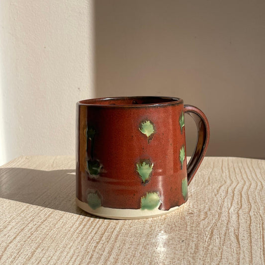 Red ceramic mug with green spots on a wooden surface
