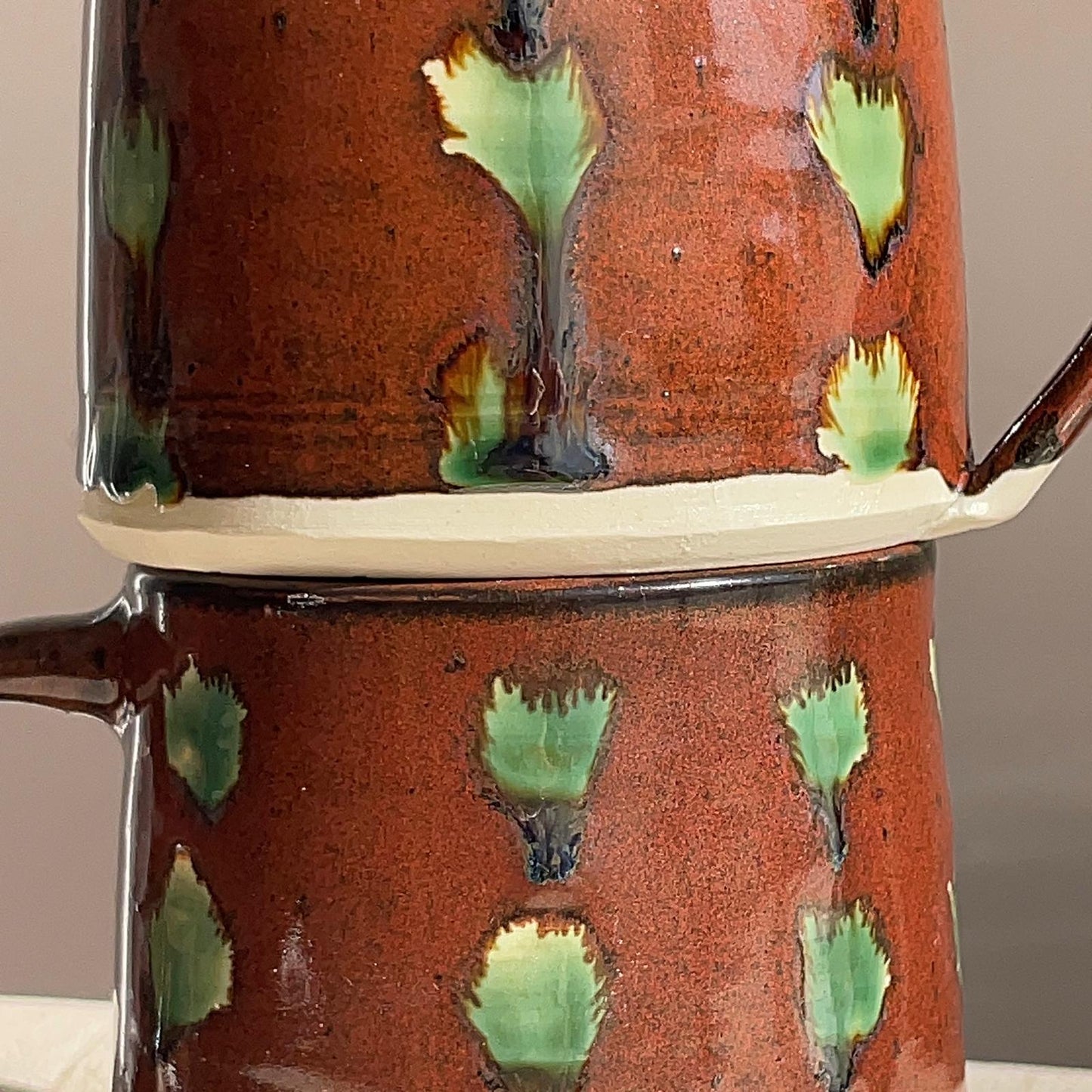 Ceramic mug with green leaf patterns on a neutral background