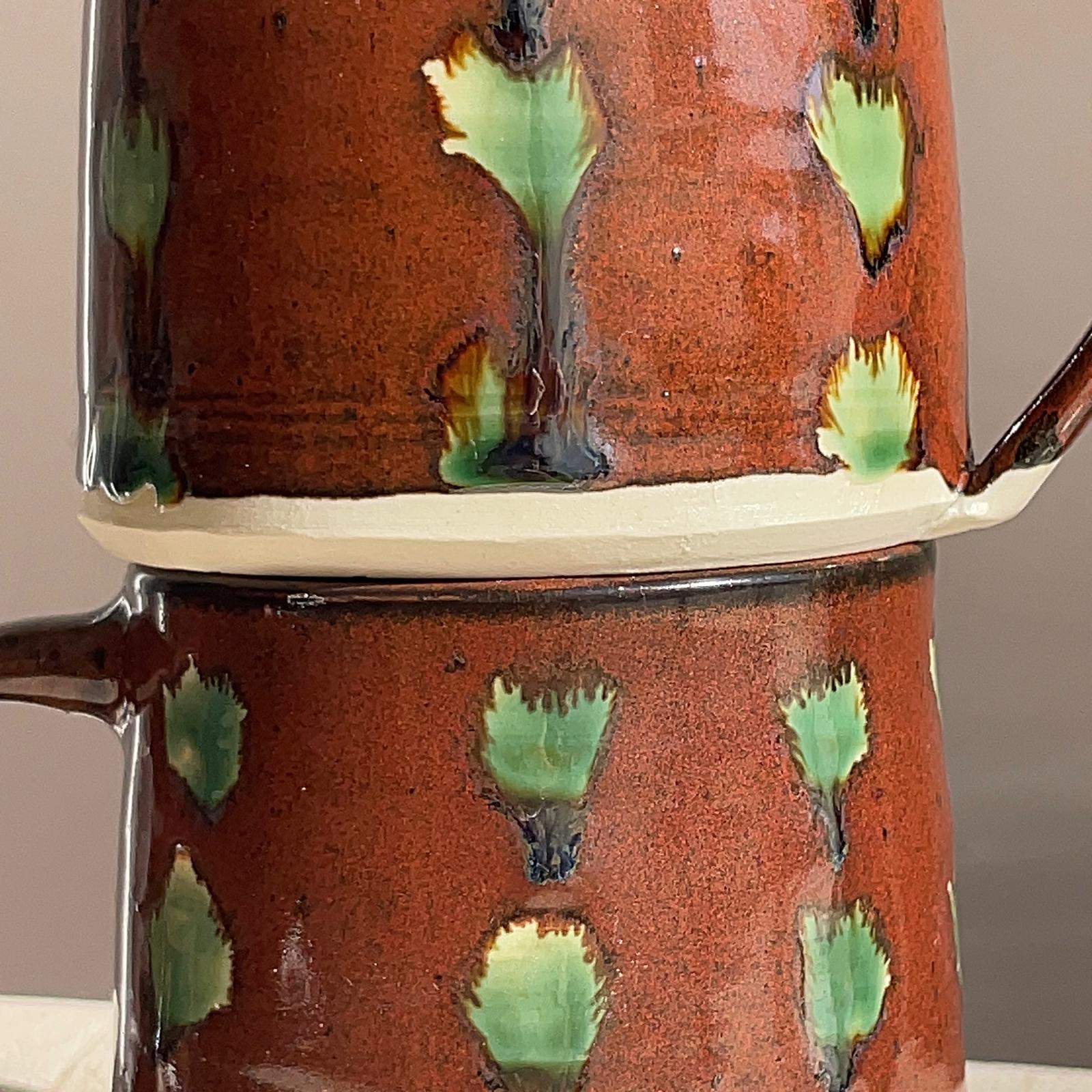 Ceramic mug with green leaf patterns on a neutral background