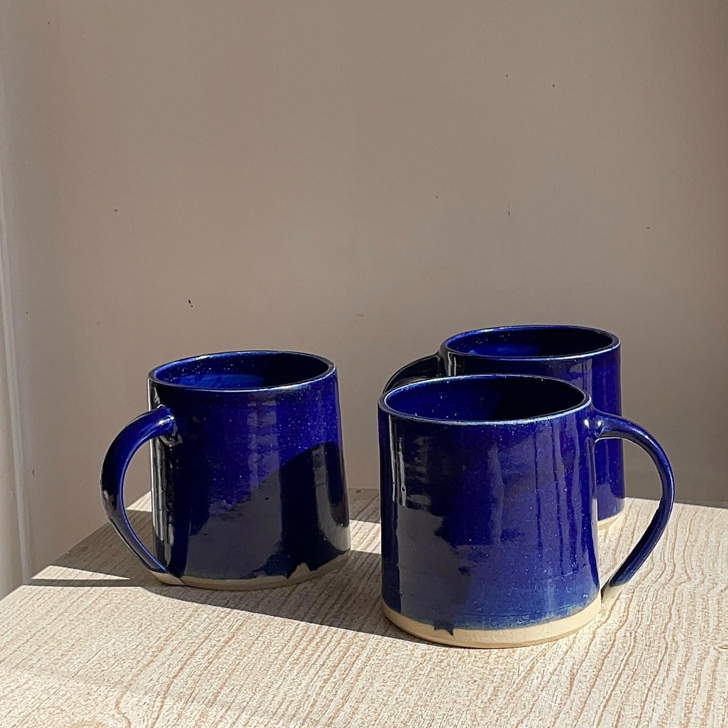 Three blue ceramic mugs on a wooden surface with a neutral background
