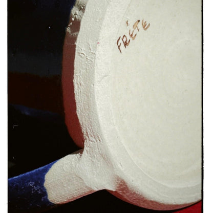 Close-up of a white ceramic pot with 'frete' branding on a dark background