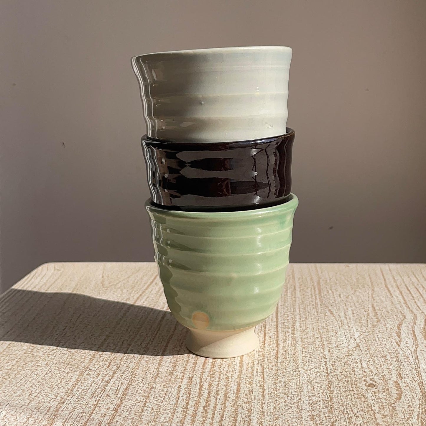 Stack of three ceramic pots in green, black, and white on a wooden surface with a gray background