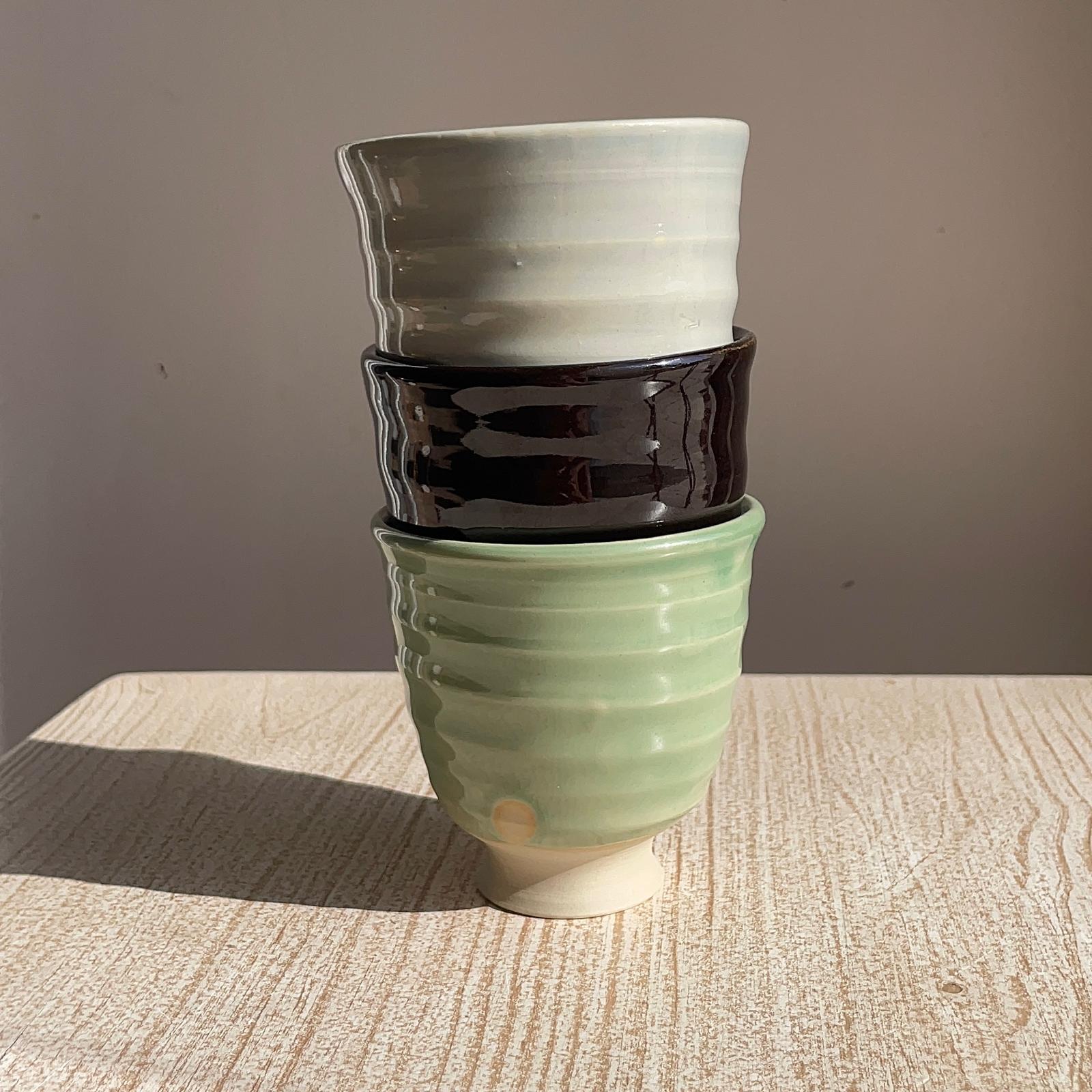 Stack of three ceramic pots in green, black, and white on a wooden surface with a gray background