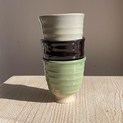 Stack of three ceramic pots in green, black, and white on a wooden surface with a gray background