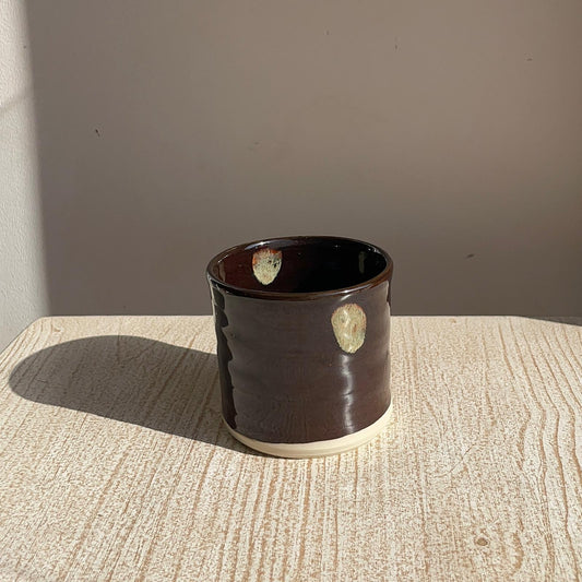Brown ceramic cup with circular patterns on a textured surface
