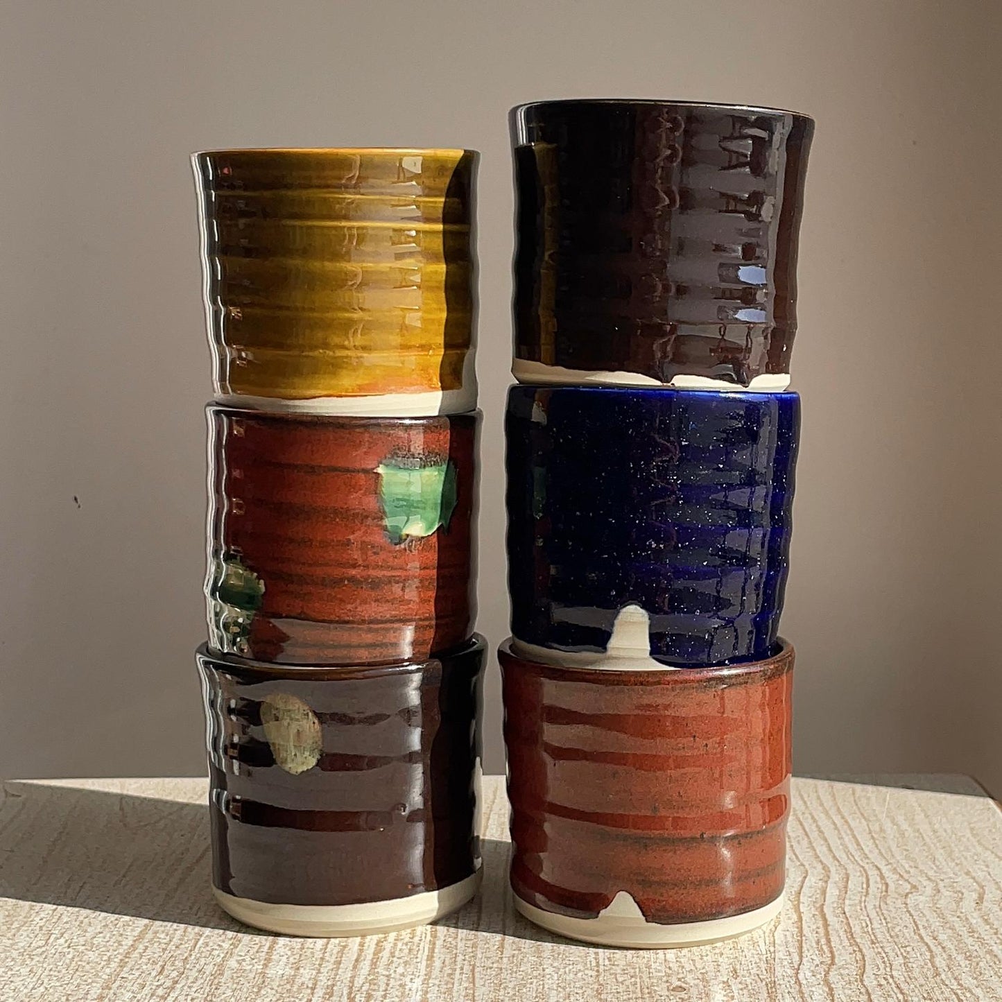 Stack of colorful ceramic cups on a textured surface with a neutral background