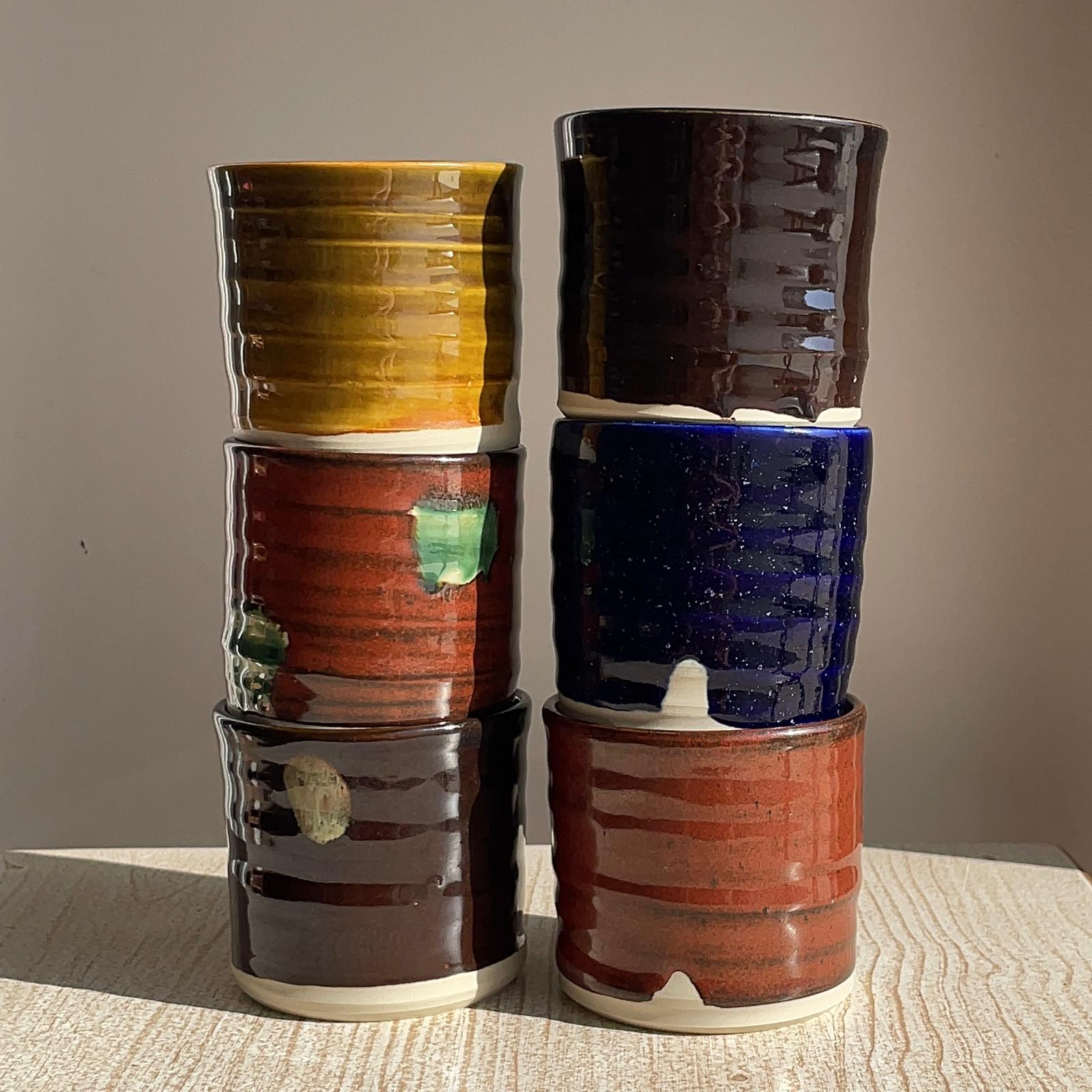 Stack of colorful ceramic cups on a textured surface with a neutral background