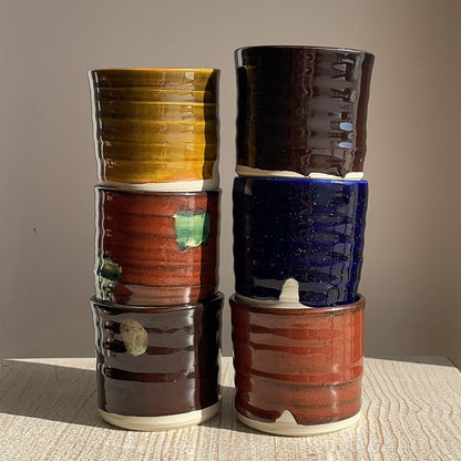 Stack of colorful ceramic cups on a textured surface with a neutral background
