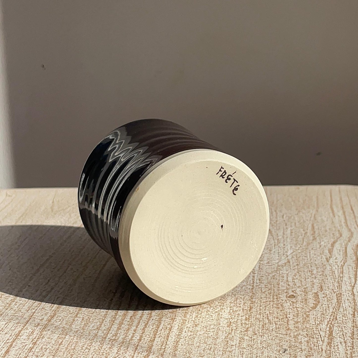 Ceramic cup with black glaze and 'Frete' branding on a wooden surface