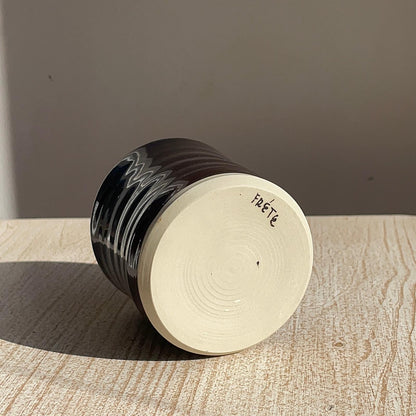 Ceramic cup with black glaze and 'Frete' branding on a wooden surface