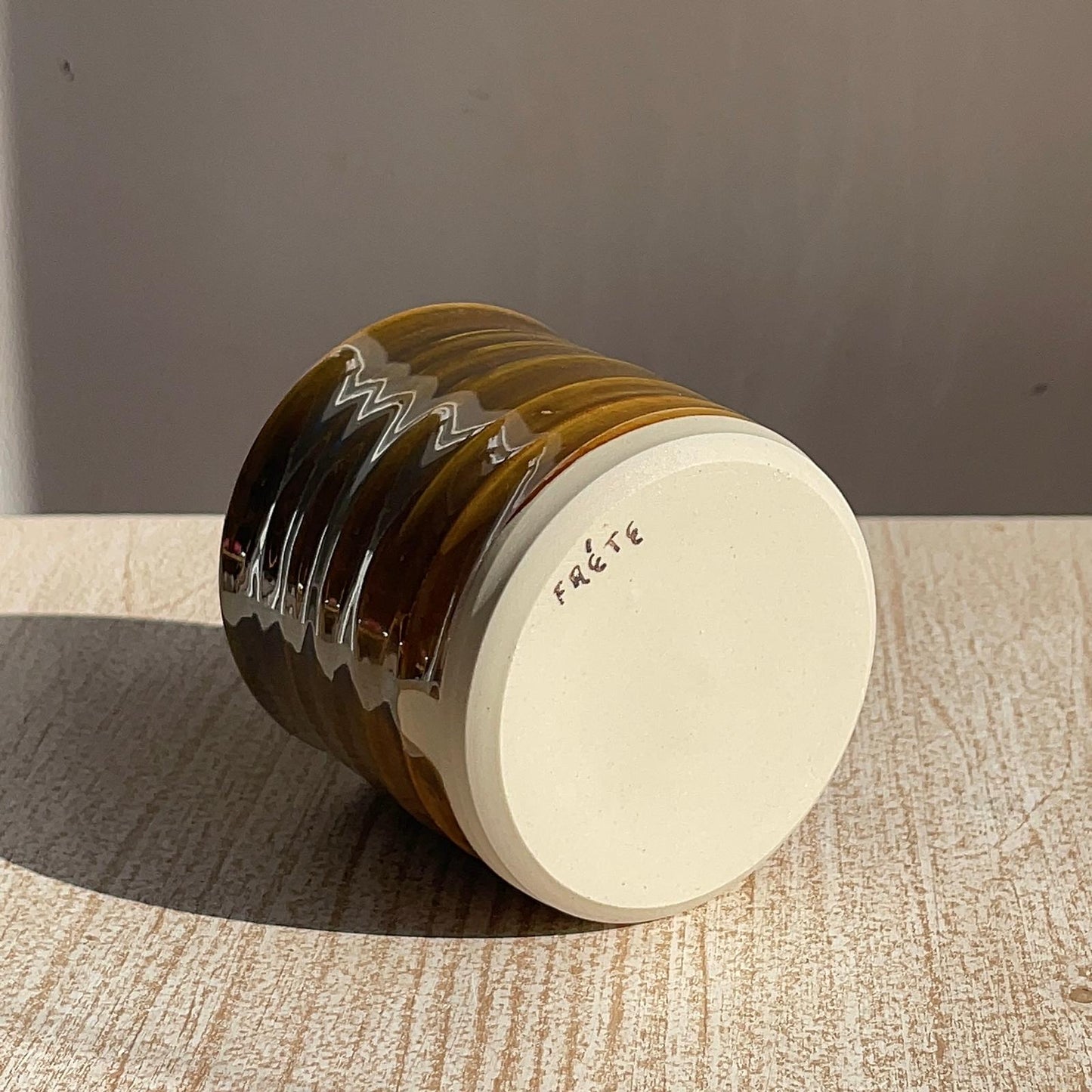 Brown ceramic cup with 'Frete' branding on a textured surface 