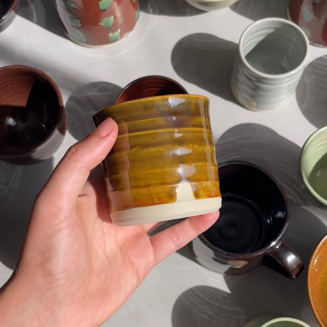 Hand holding a striped ceramic cup with other ceramic items on a light surface