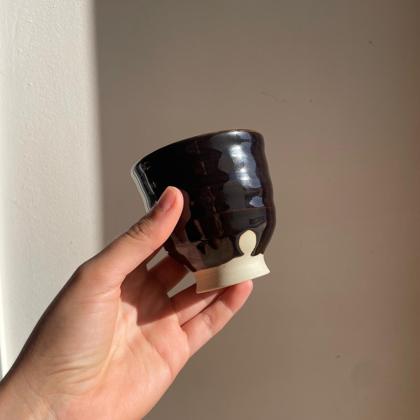 Hand holding a black ceramic cup  against a plain background