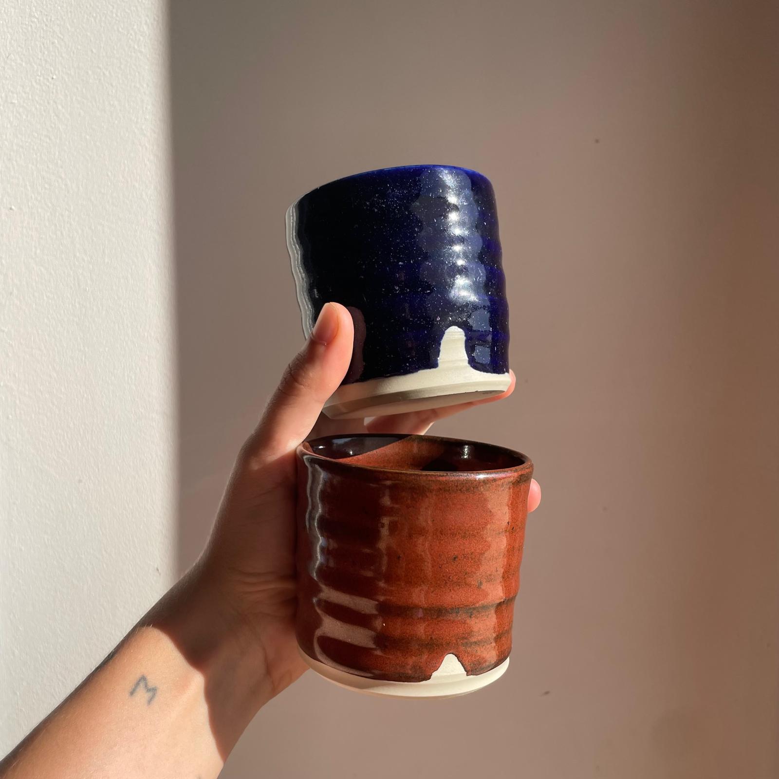 Hand holding two ceramic cups, one blue and one red , against a plain background