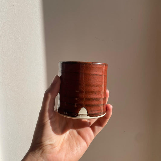 Hand holding a red ceramic cup against a plain background
